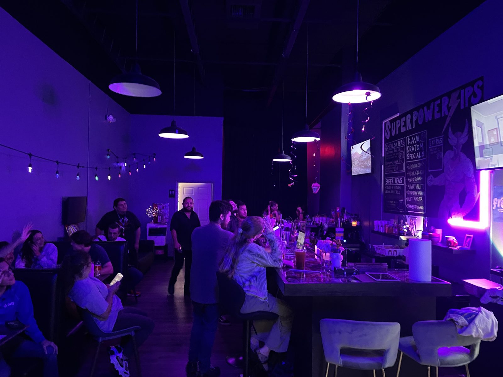 Komic Kava bar at night with purple lighting, full bar seating and the Superpower Sips chalkboard menu
